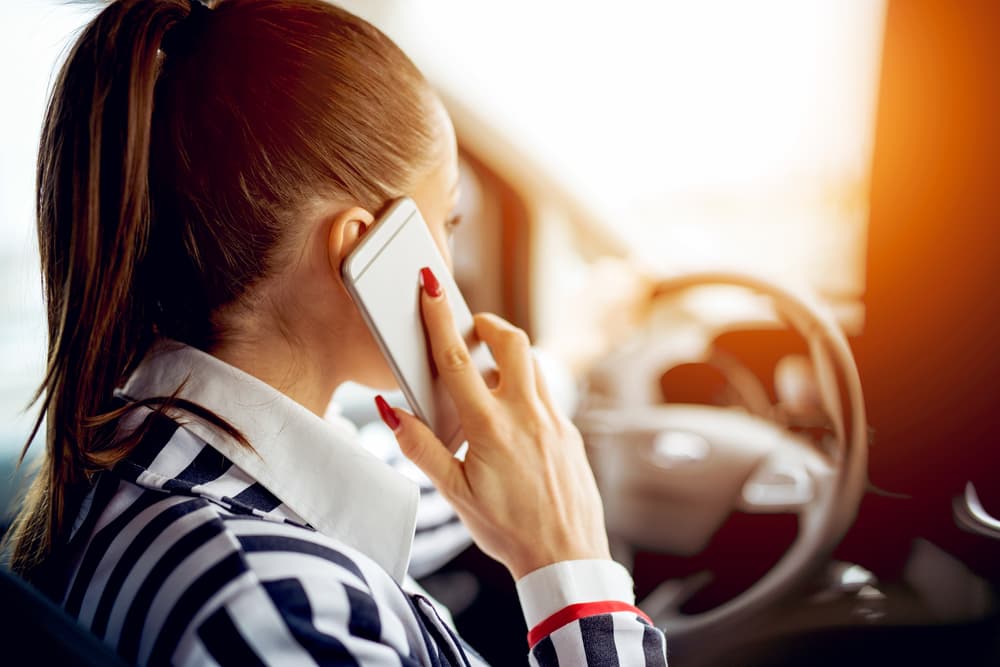 A precarious scenario unfolds as a young woman drives her car while distractedly talking on her smartphone.