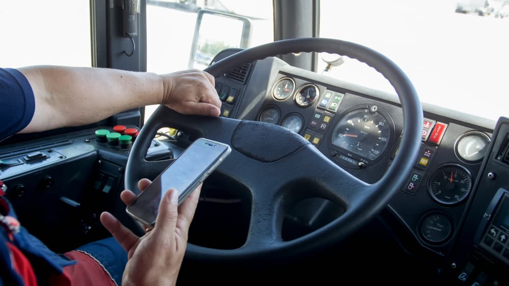 A close-up photo of an irresponsible man typing a phone number while driving a truck, highlighting the danger in transport caused by an inattentive driver.






