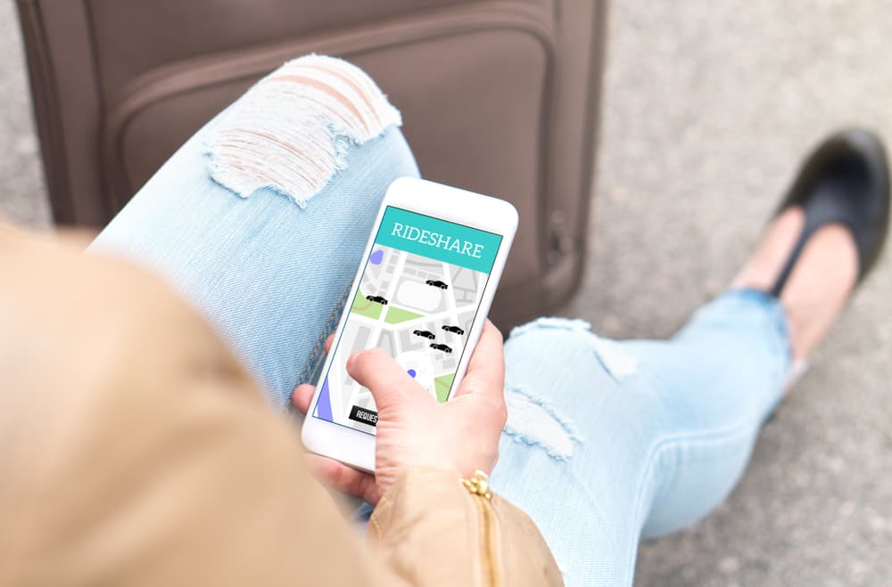 A young woman using a rideshare app on her smartphone to order a taxi or carpool ride while traveling.