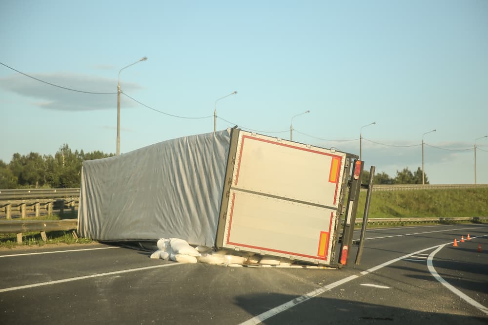 Back view of an overturned truck on the highway with bags spilled out. Accident on the road.