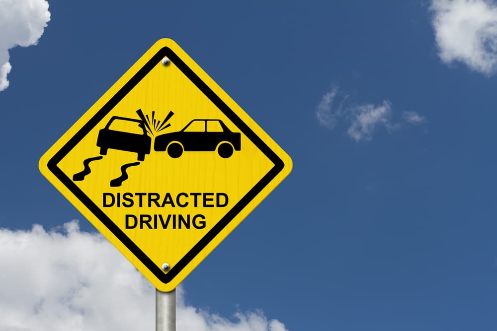 No Distracted Driving Sign: Yellow warning sign with the words "Distracted Driving" and an accident icon against a sky background.