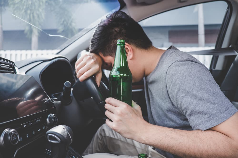 A young Asian man drives a car while holding a bottle of beer and falls asleep behind the wheel.






