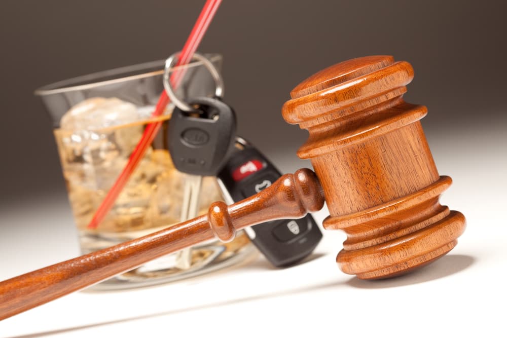 Gavel, alcoholic drink, and car keys arranged on a gradient white background—highlighting the serious consequences of drinking and driving.