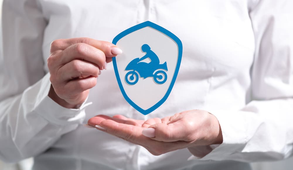 Concept of motorbike insurance with paper shield held by a female hand.






