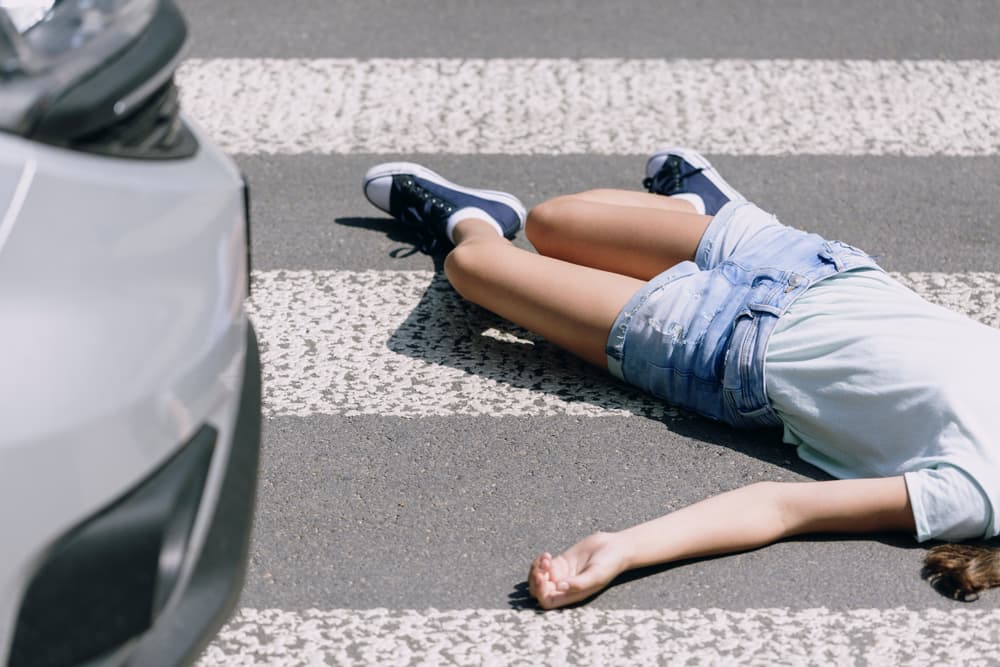 Teenage schoolkid lying on the street after a severe car crash at a pedestrian crossing.