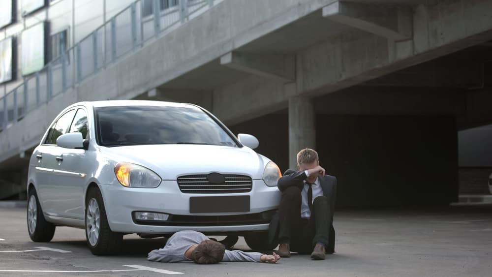 Desperate male driver sits by the road next to an unconscious pedestrian, facing a dangerous situation.