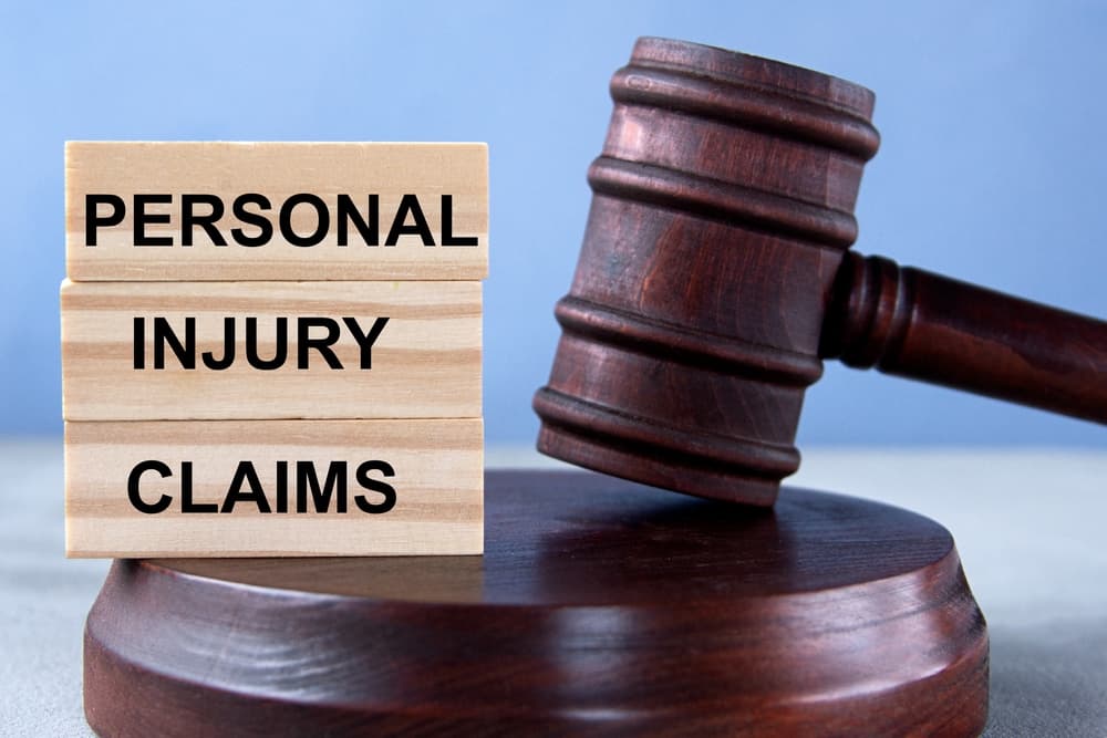 The words "PERSONAL INJURY CLAIMS" on wooden cubes, set against the backdrop of a judge's gavel and stand. Business concept.