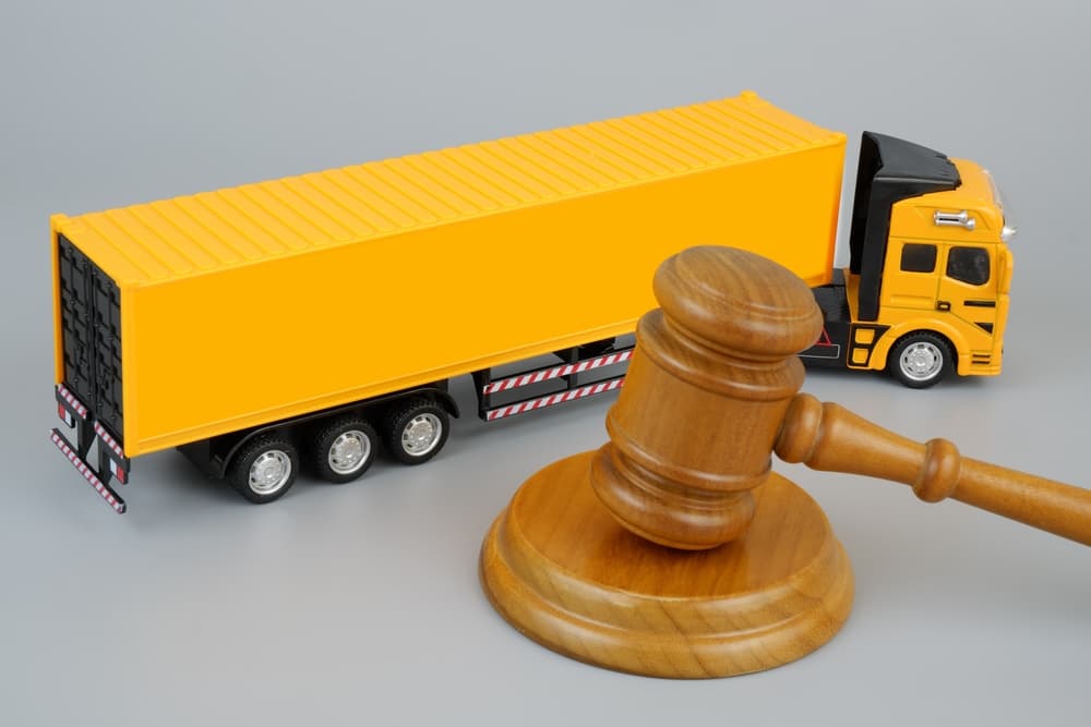 Wooden gavel and yellow cargo truck on a grey background. Legal and transportation concept.






