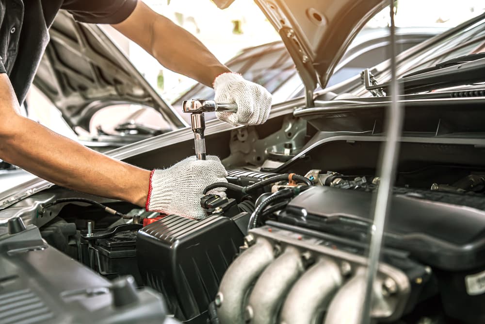 Close-up of an auto mechanic's hands using a wrench to repair and maintain a problematic auto engine at a car repair shop.