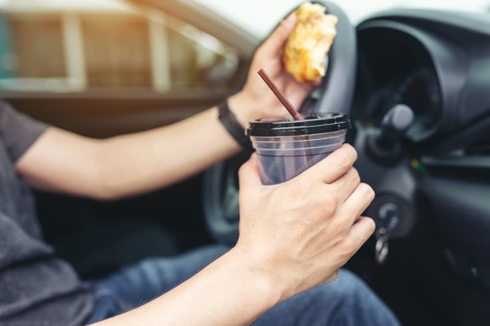 Man Eating Pizza and Drinking Coffee While Driving a Car.






