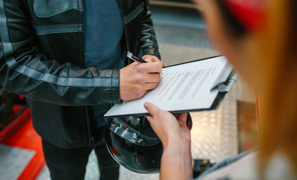 Unrecognizable biker man wearing a leather jacket and holding a helmet, signing an insurance policy to receive his repaired motorcycle at the workshop.