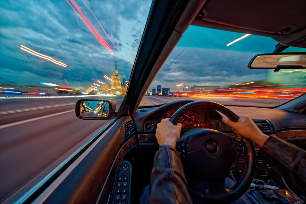 Movement of a car at night at high speed, viewed from the interior with the driver's hands on the wheel. Concept of the speed of life. Long exposure photo.






