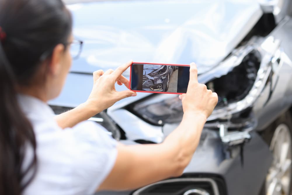 Woman taking photos of car damage with a smartphone after an accident.