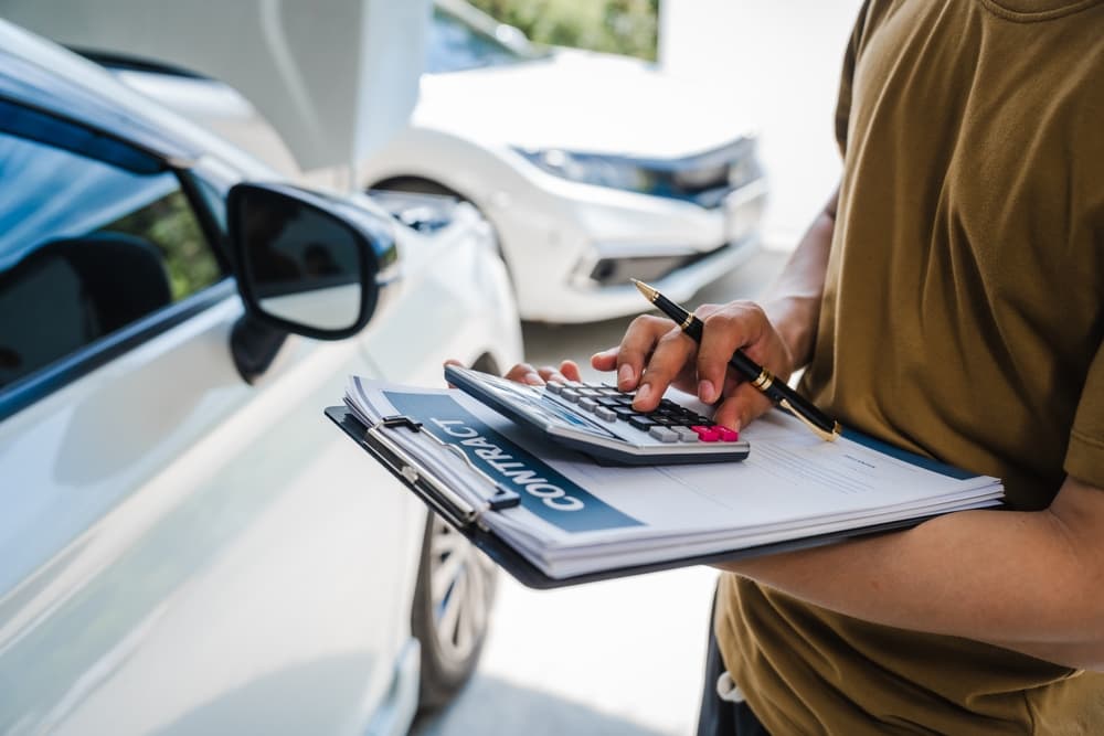 A man fills out a car insurance form after an accident. Comprehensive motor insurance covers the damage, and he files a claim while discussing details with an adjuster.