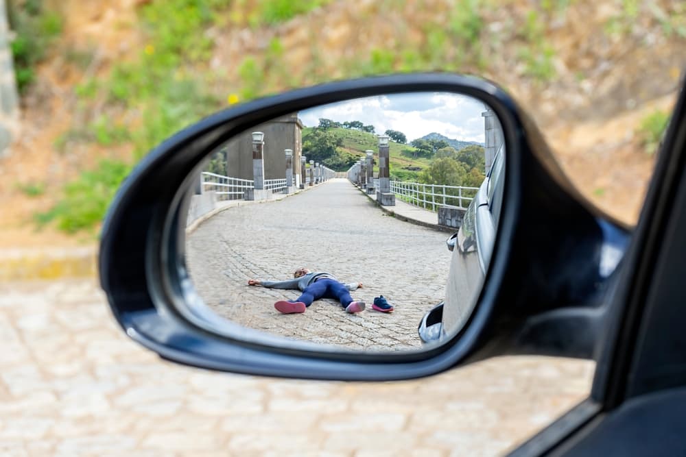 Pedestrian fatality seen through a rearview mirror, with the victim lying motionless on the road after being run over. 