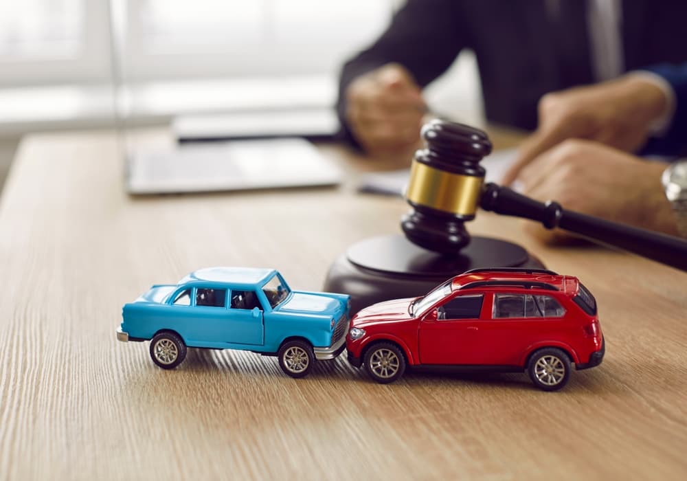 Gavel and two small toy car models on desk in courthouse.