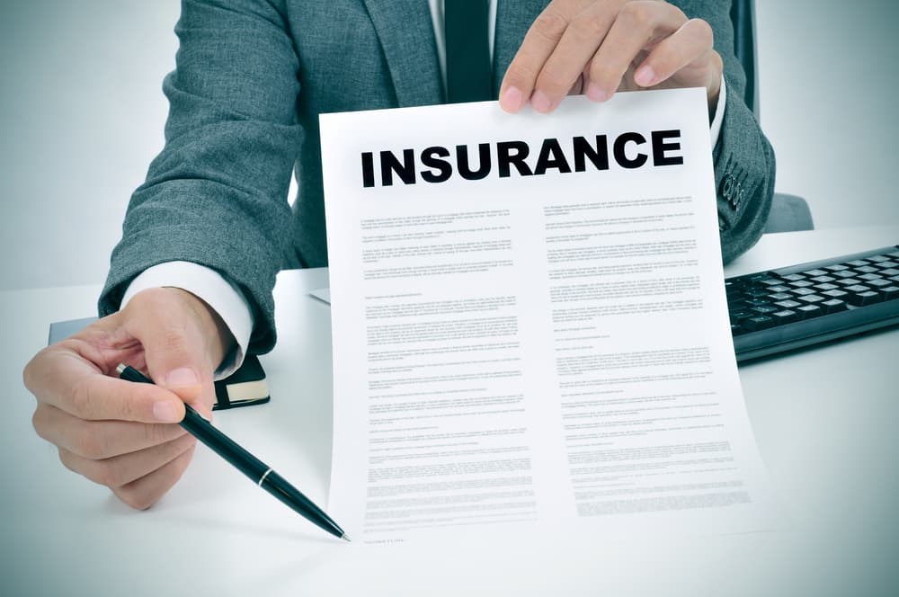 young man in suit in his office showing an insurance policy and pointing with a pen where the policyholder must to sign