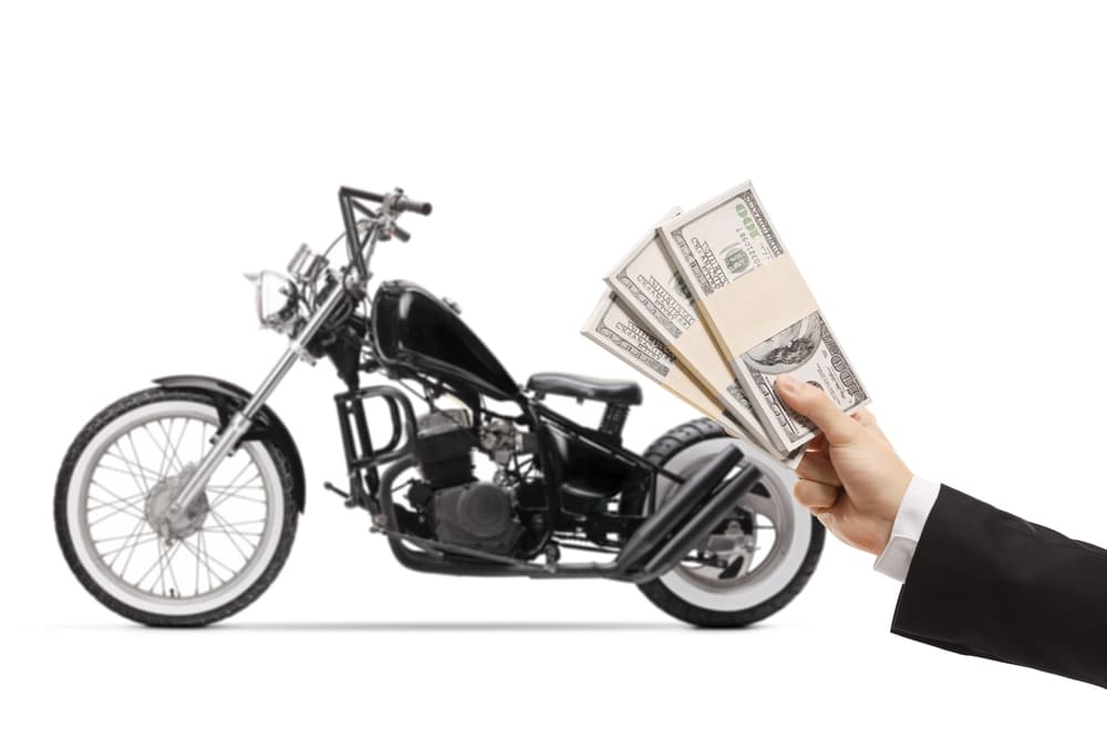 Man holding cash with a motorcycle in the background